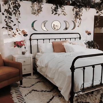 Beige moon mirrors arranged in lunar order above a cozy bed with fairy lights