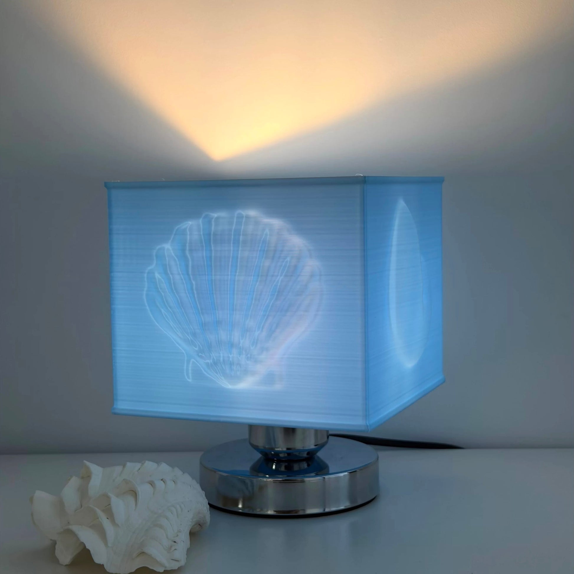 Table lamp with shell design on the shade, next to a white shell on a light background