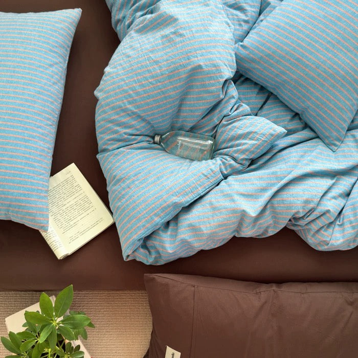 Blue striped comforter on a bed with pillows and a book in a bedroom setting.