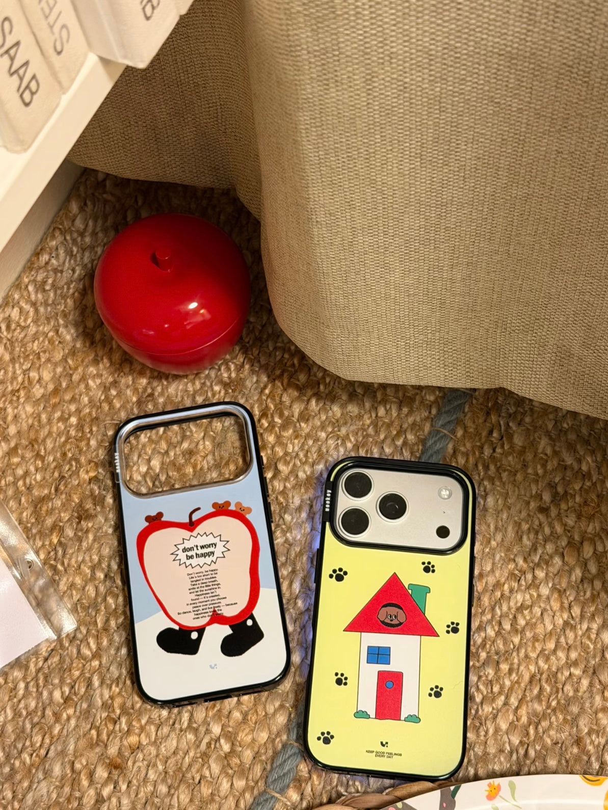 Blue apple and yellow house acrylic phone case designs sit together, each surrounded by a black border.