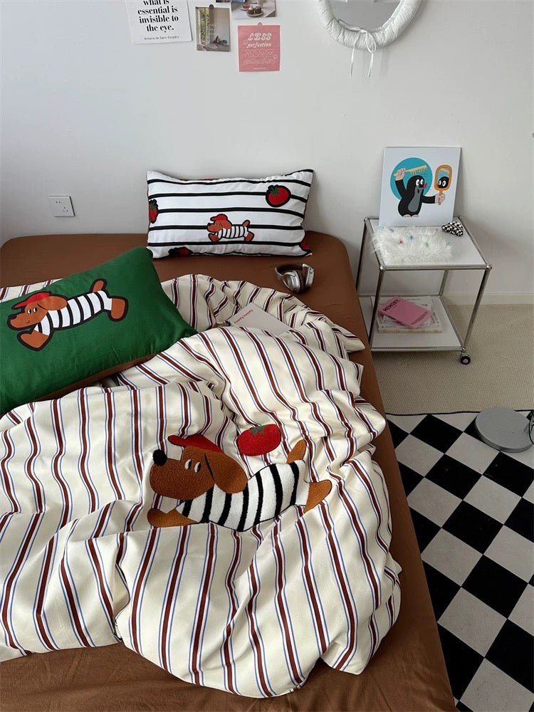 Bed with striped bedding and cartoon dog design, green pillow, and small table with decor items.
