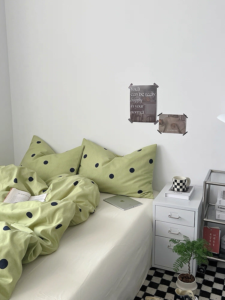 Bed with green polka dot bedding and a white nightstand in a room.