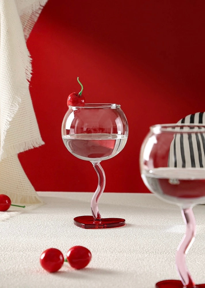 Two heart-shaped wine glasses with red cherries on a white surface.