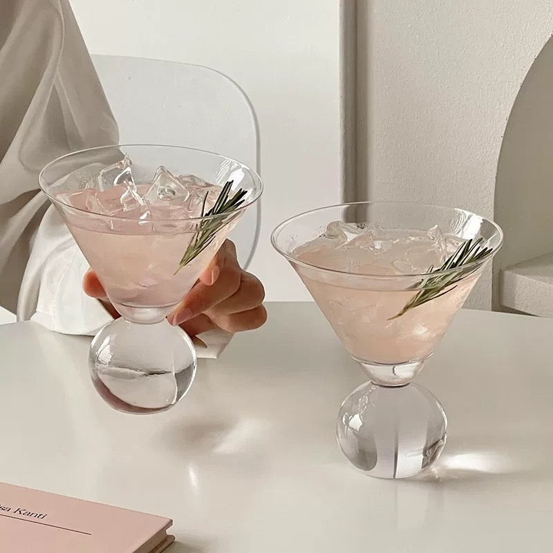 Two pink cocktails with ice and a sprig of rosemary in clear glasses on a white surface.