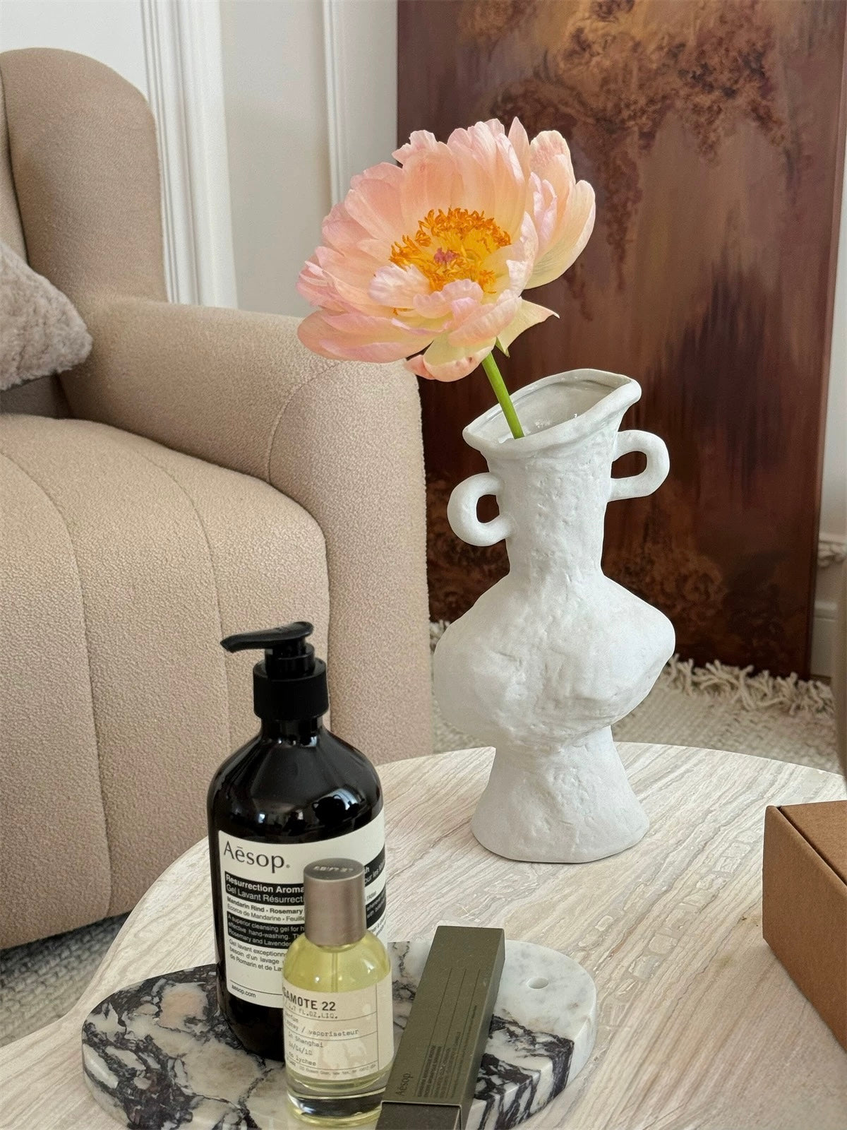 Aesop products on a marble coaster with a vase and flower in the background.