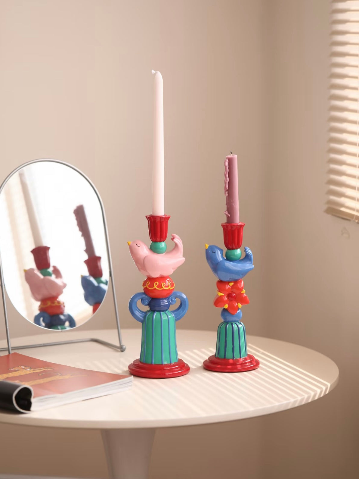 Pink and blue bird candle holders shown together in a close-up view on a light stone table.