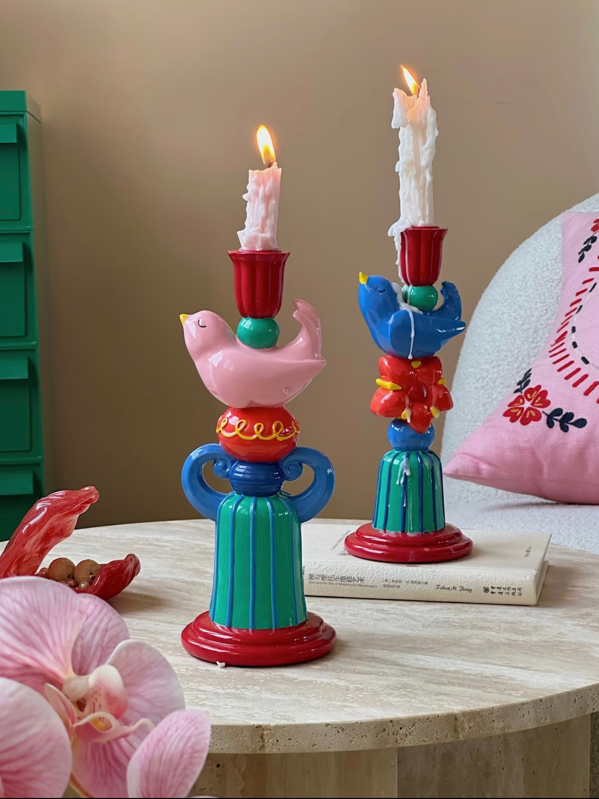 Pink and blue bird candle holders with lit candles styled on a coffee table beside books and flowers.
