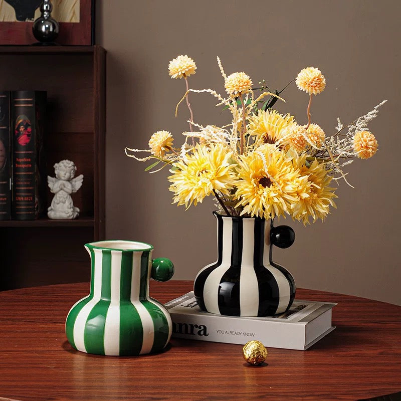 Two decorative vases with a black and white striped pattern and green and white striped pattern, containing yellow flowers on a wooden surface.