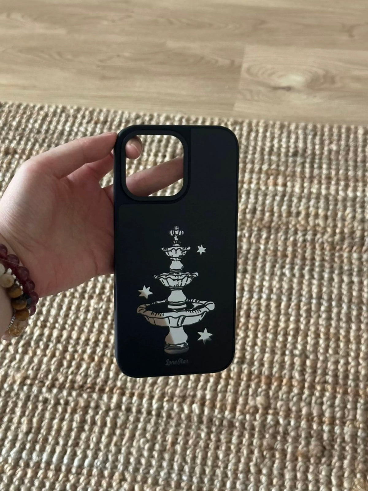 A black fountain phone case held upright, with the tiered fountain and scattered stars fully visible.
