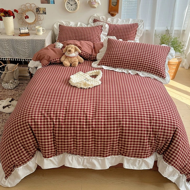 Red and white checkered bedspread with decorative pillows and a teddy bear on a bed in a bright room.