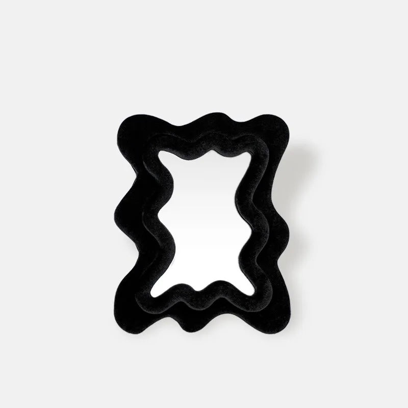 A black wavy-edged mirror with a plush velvet-like finish, shown from a top-down perspective on a light gray background.