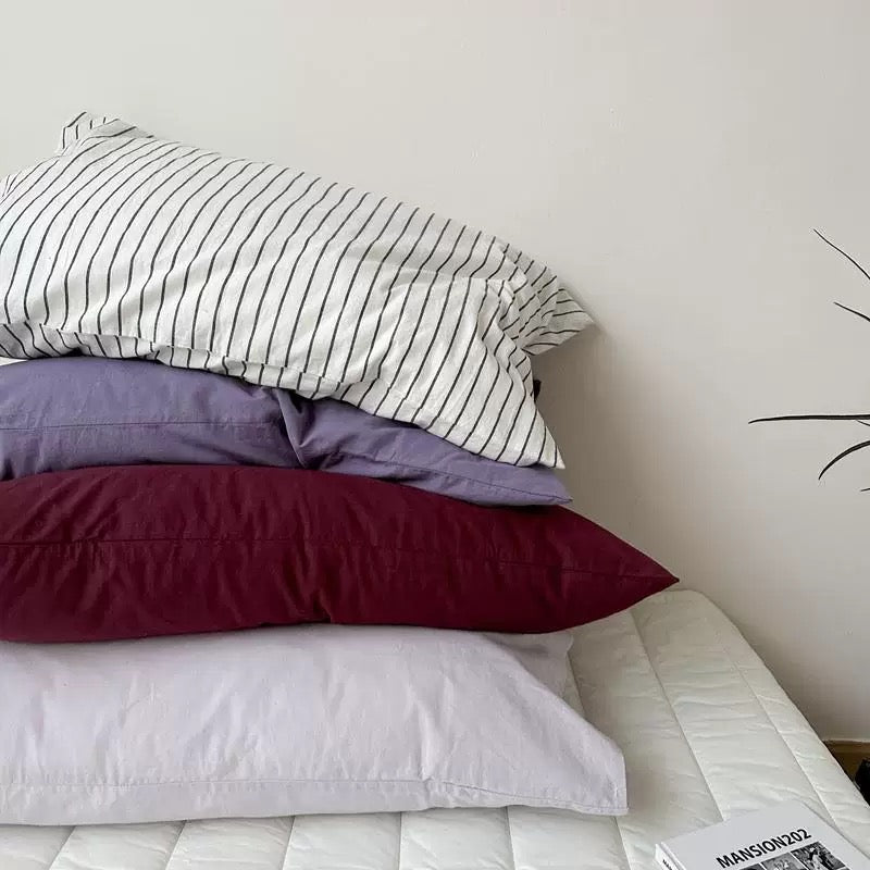 A black and white striped pillowcase sits on a stack with lavender, plum, and pale gray designs.