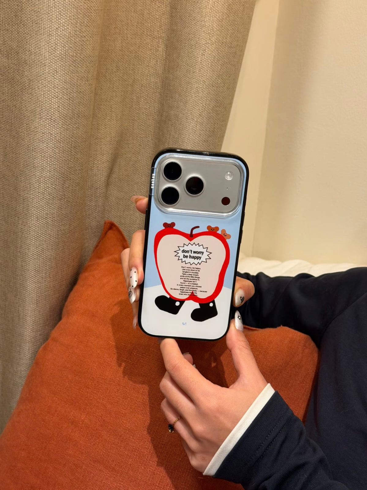 A blue apple phone case is held upright, showing little bears above a red apple character with black feet.