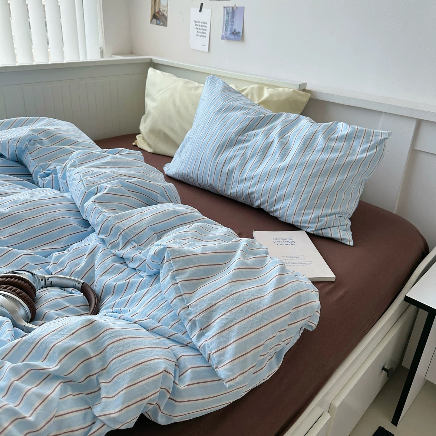 Bed with blue striped bedding and pillows in a room with a window and desk.
