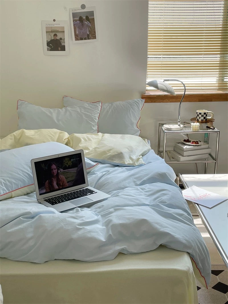 Laptop on a bed with a nightstand and window blinds in the background