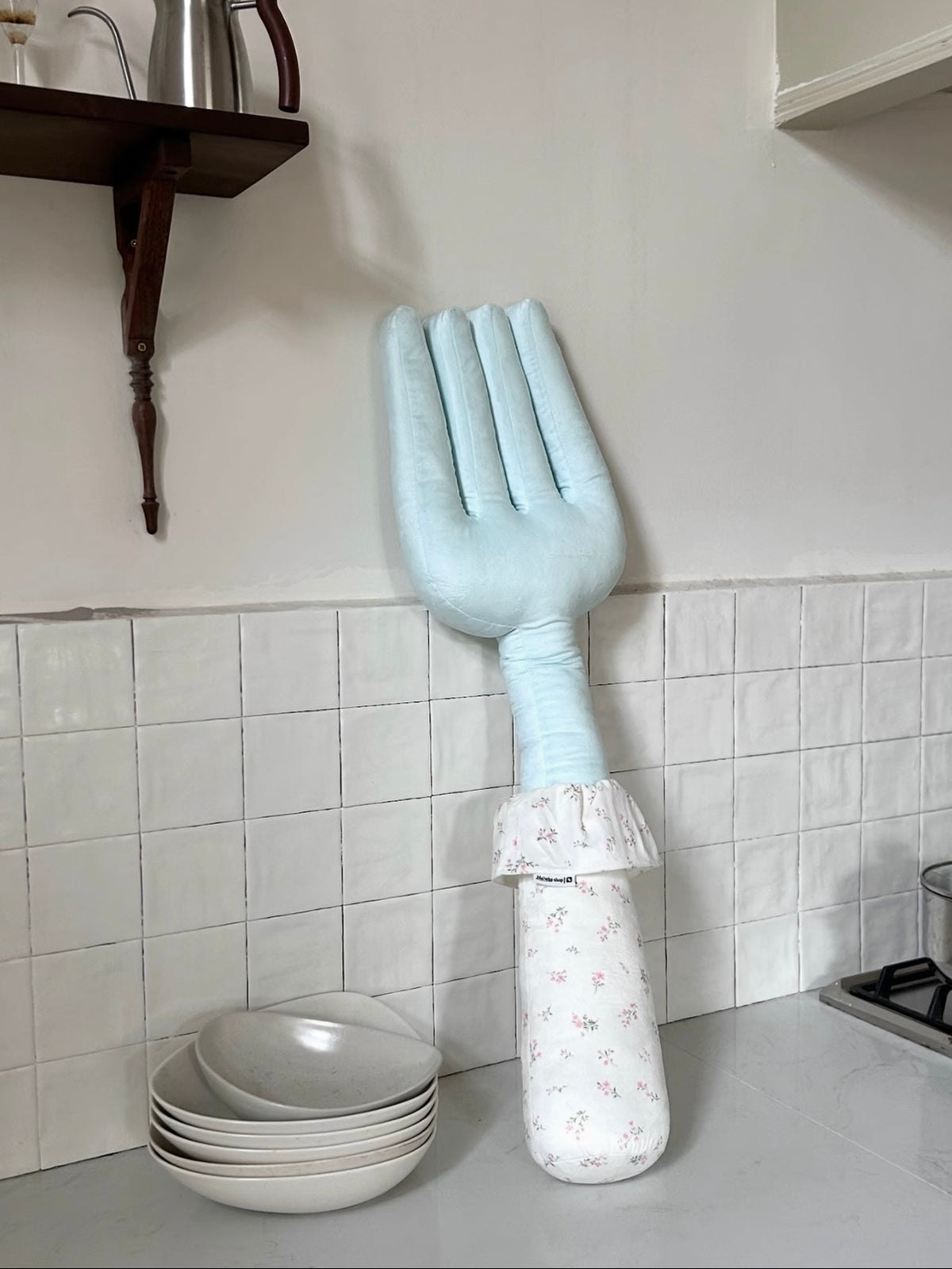 A blue fork pillow stands on a counter, with its pale floral handle below the gathered fabric collar.