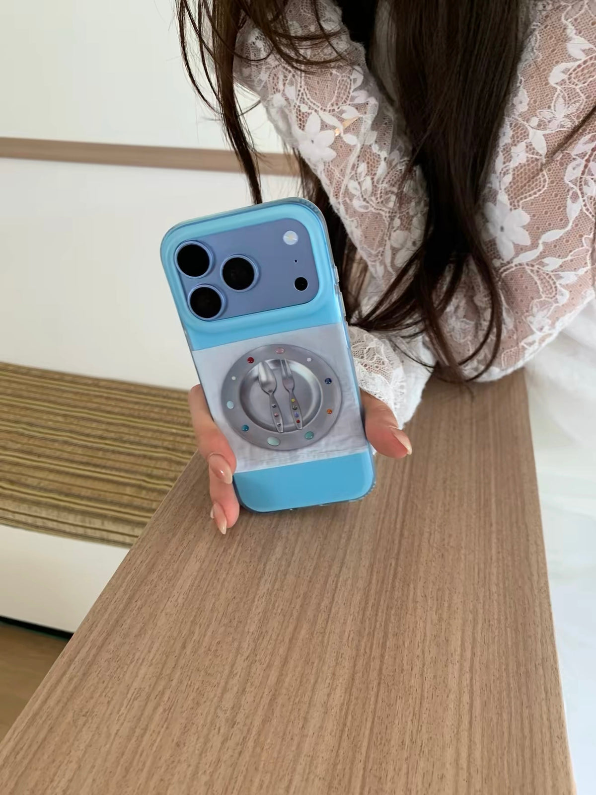 A blue iPhone case held upright in one hand, with a large plate and cutlery illustration below the camera.