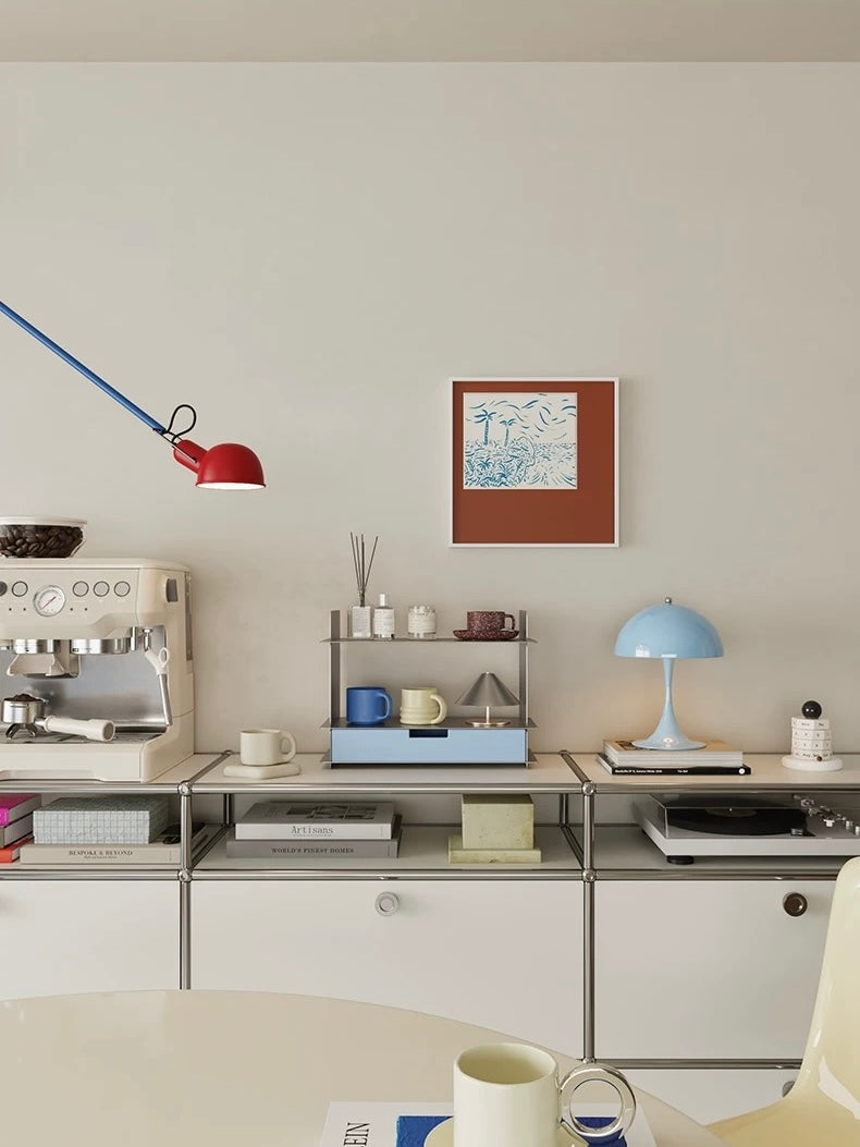 Blue perfume shelf on a white sideboard in a room with a red lamp and framed art