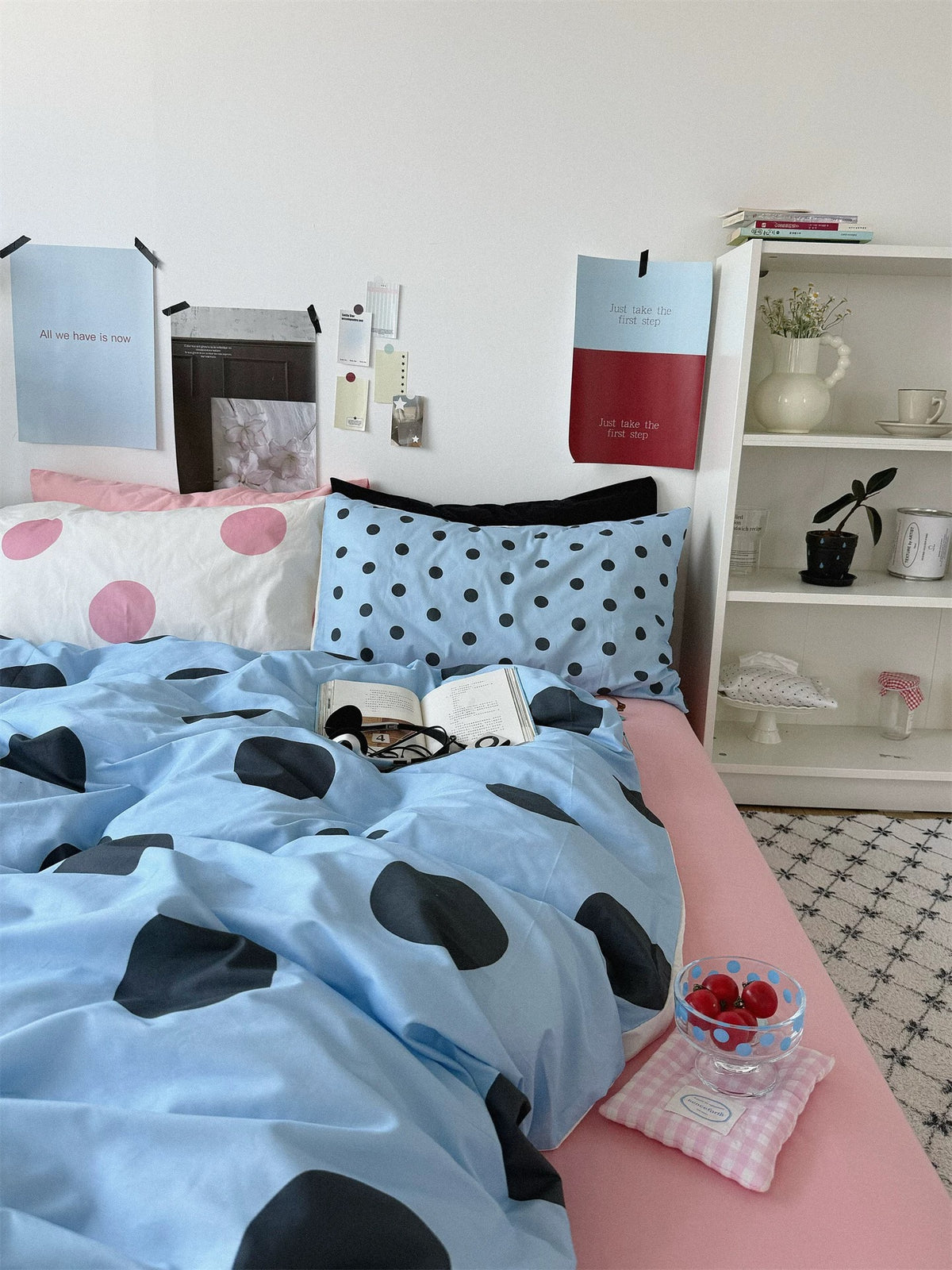 A cream pillowcase with large pink dots rests beside a small dotted blue pillow above the blue cover.