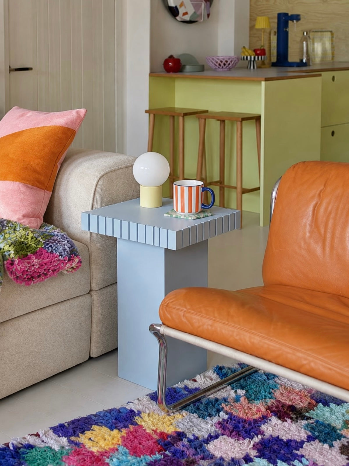 Blue sofa side table beside a beige sofa and an orange chair on a patterned rug
