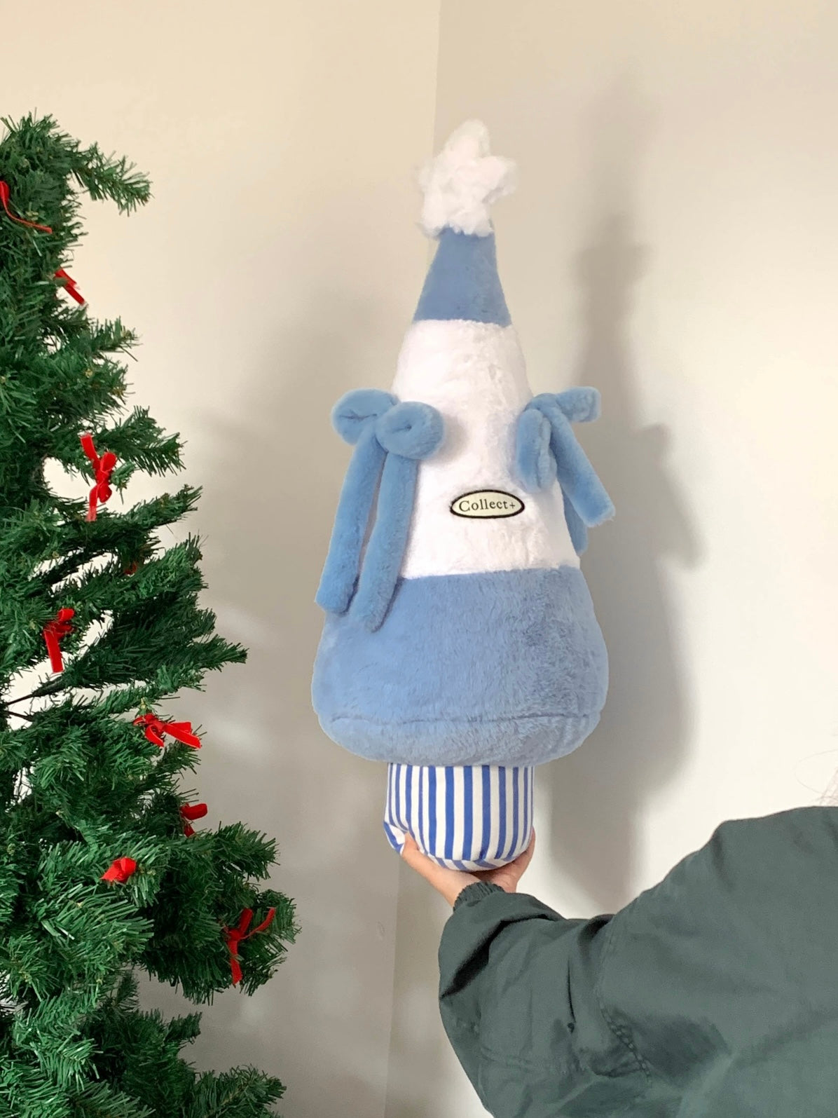 Blue and white Christmas tree cushion with plush bows beside a Christmas tree