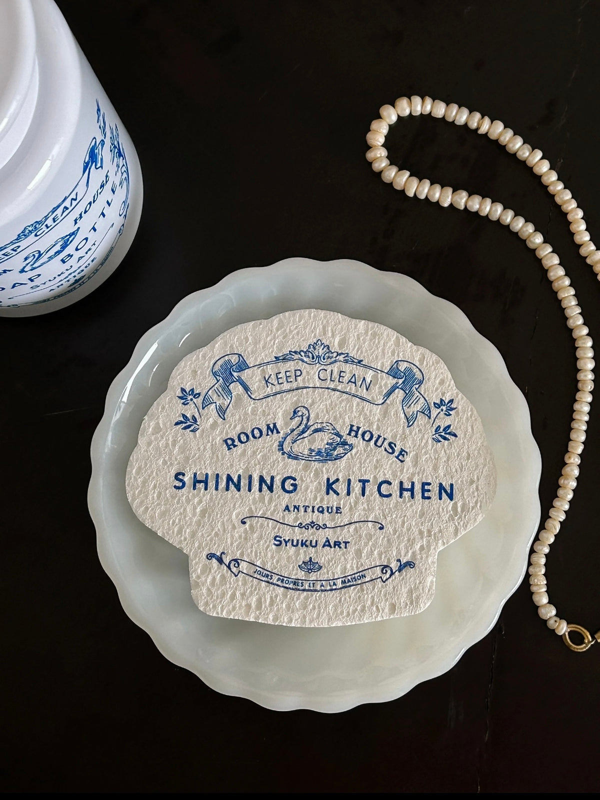A blue and white dish sponge shows its scalloped outline and swan artwork in a close view from above.