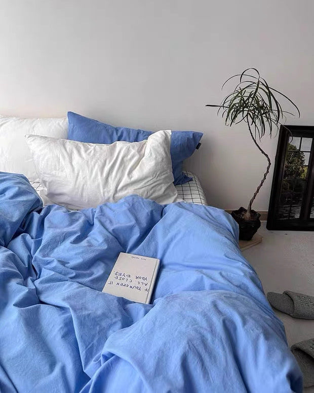 Blue bedding set on a bed with white pillows and a plant in the corner.