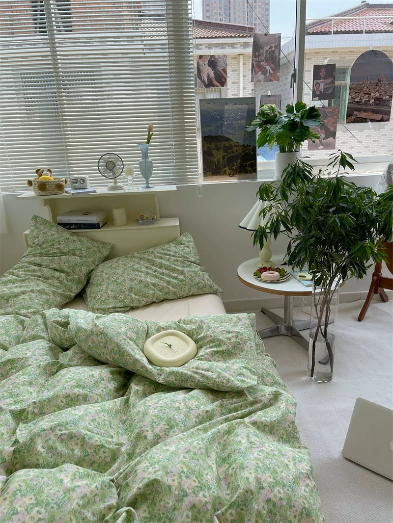 Room with green floral bedding, a plant, and a small table with items.