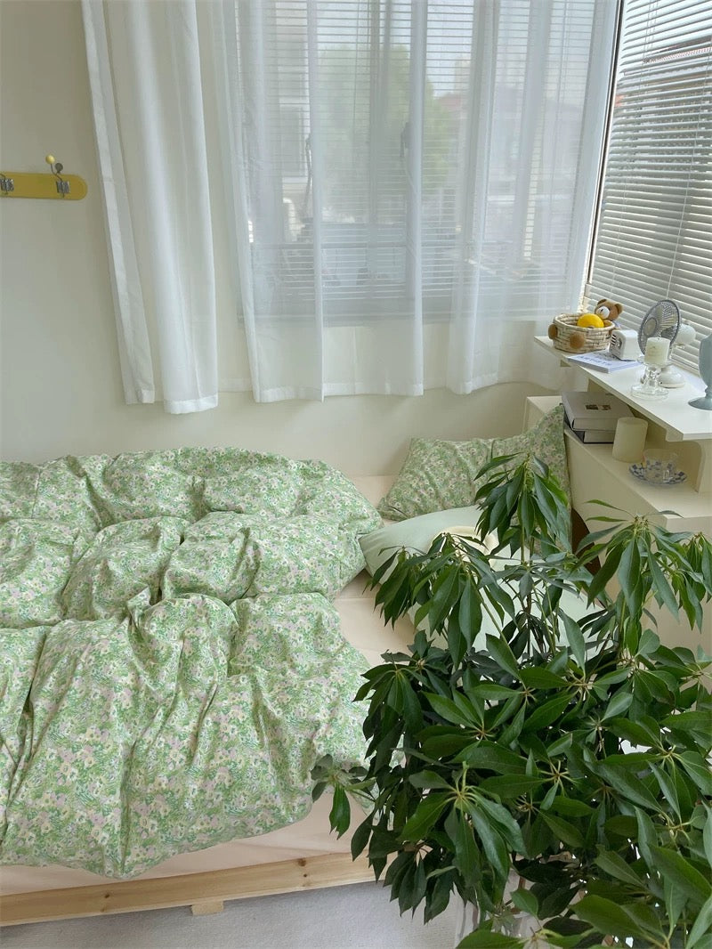 Bed with green floral bedding in a room with white curtains and a plant.