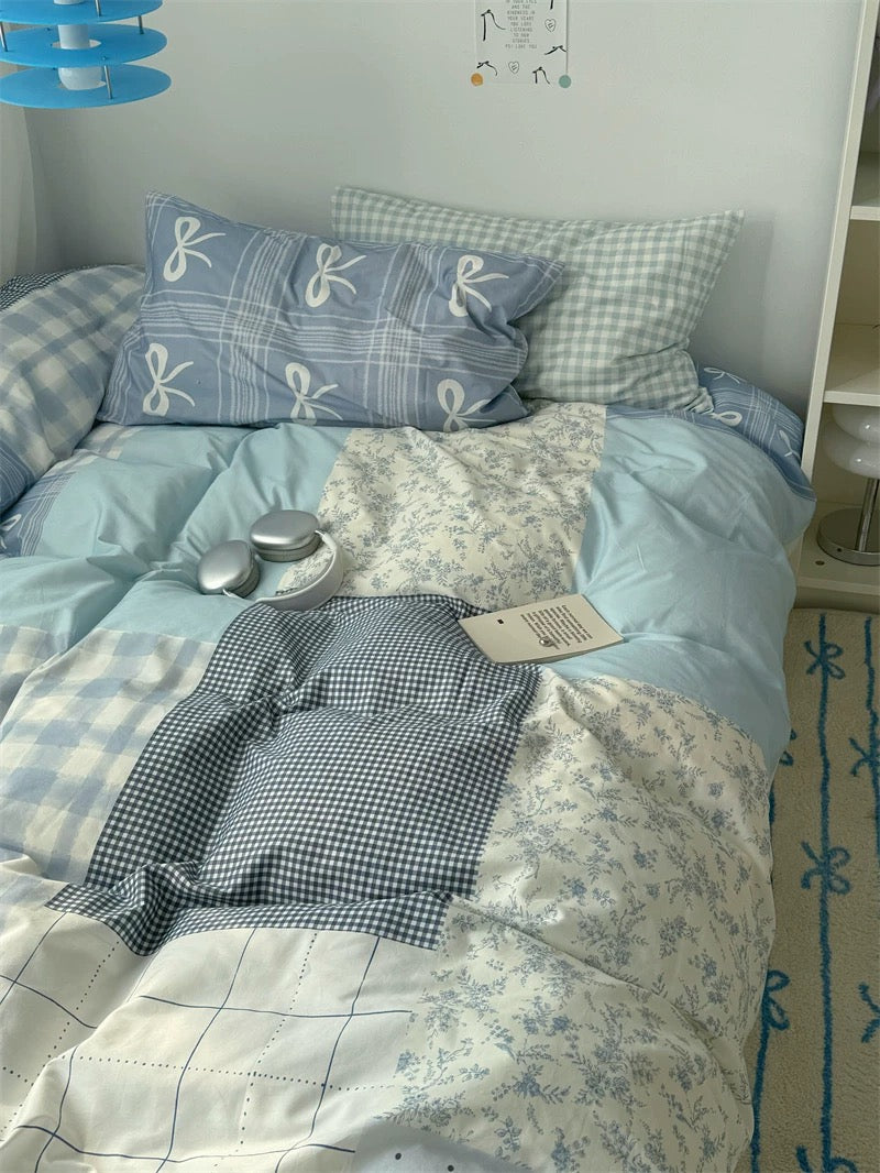 Bed with blue and white checkered bedding, pillows, and a spoon on a light-colored floor.