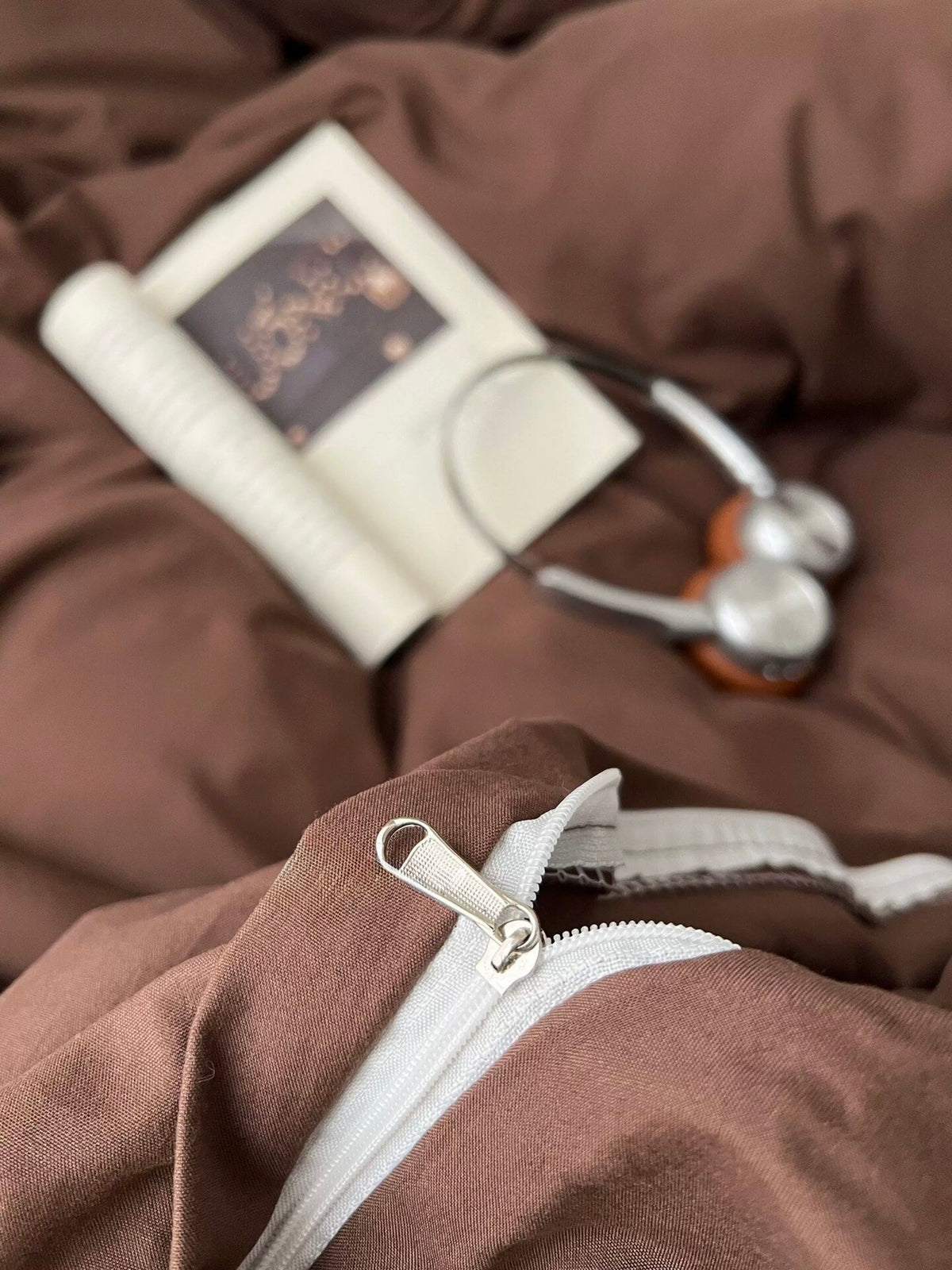 Brown duvet cover close-up with a book and headphones resting on the bed