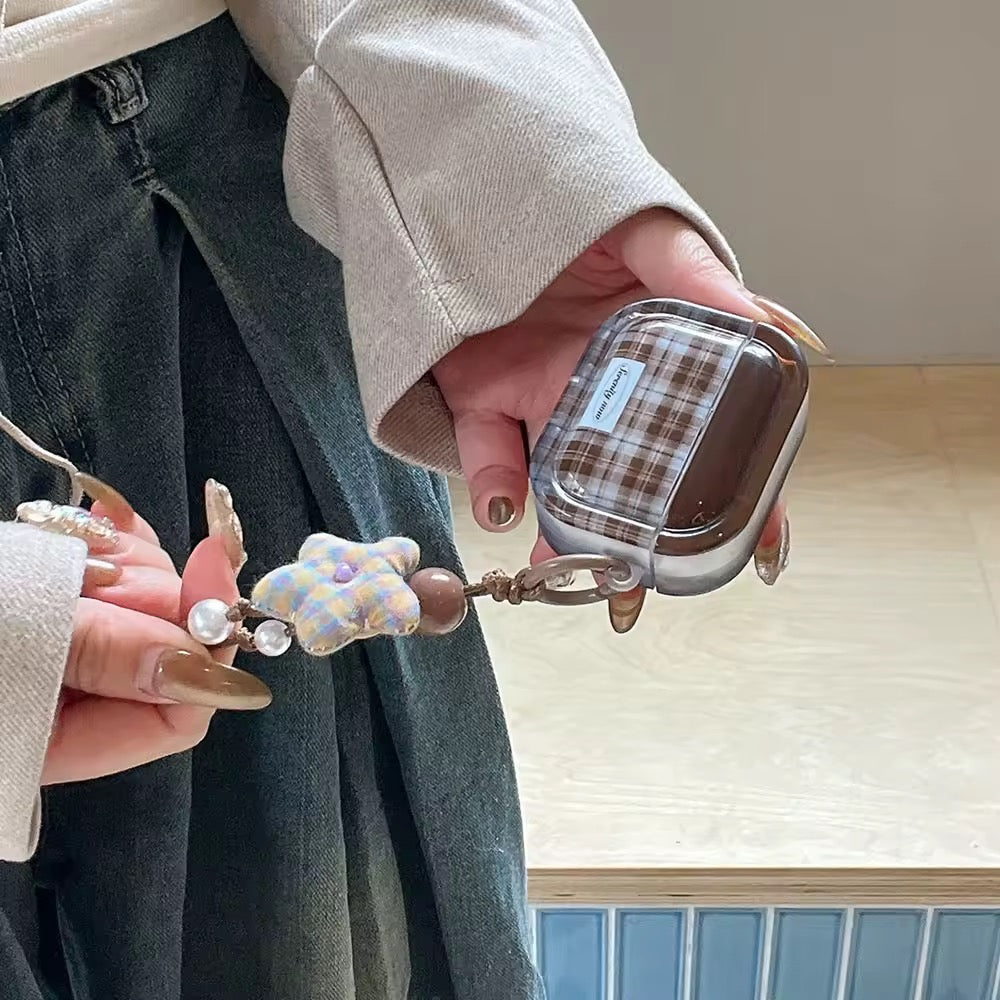 Person holding a plaid phone case with a keychain and teddy bear charm.