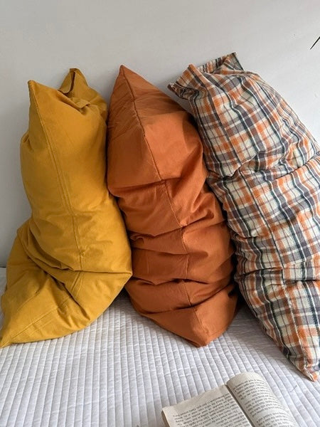 A burnt orange pillow case sits between mustard yellow and plaid designs in a leaning arrangement.