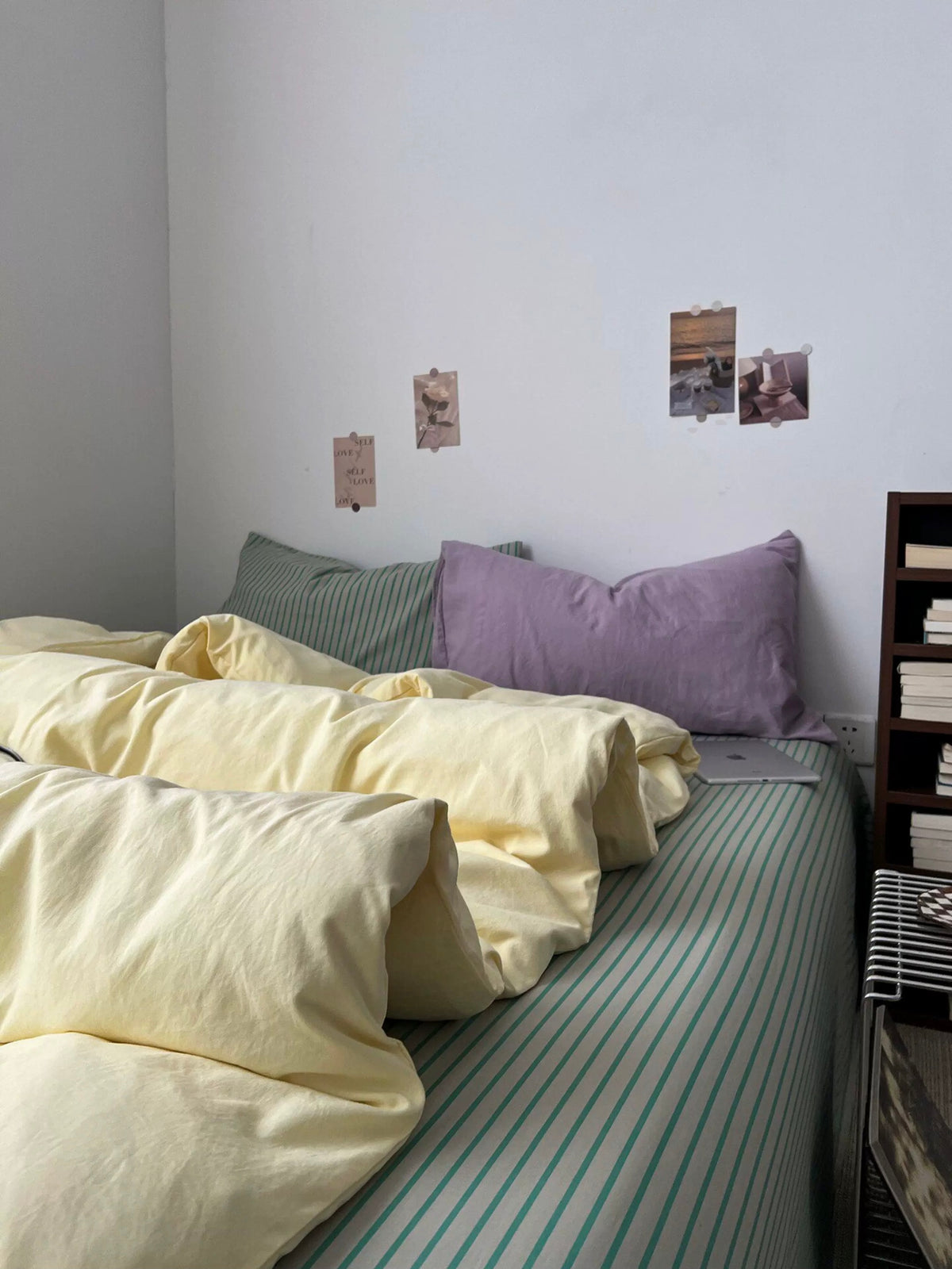 Pastel yellow bedding set spread across the bed with green striped and lilac pillows
