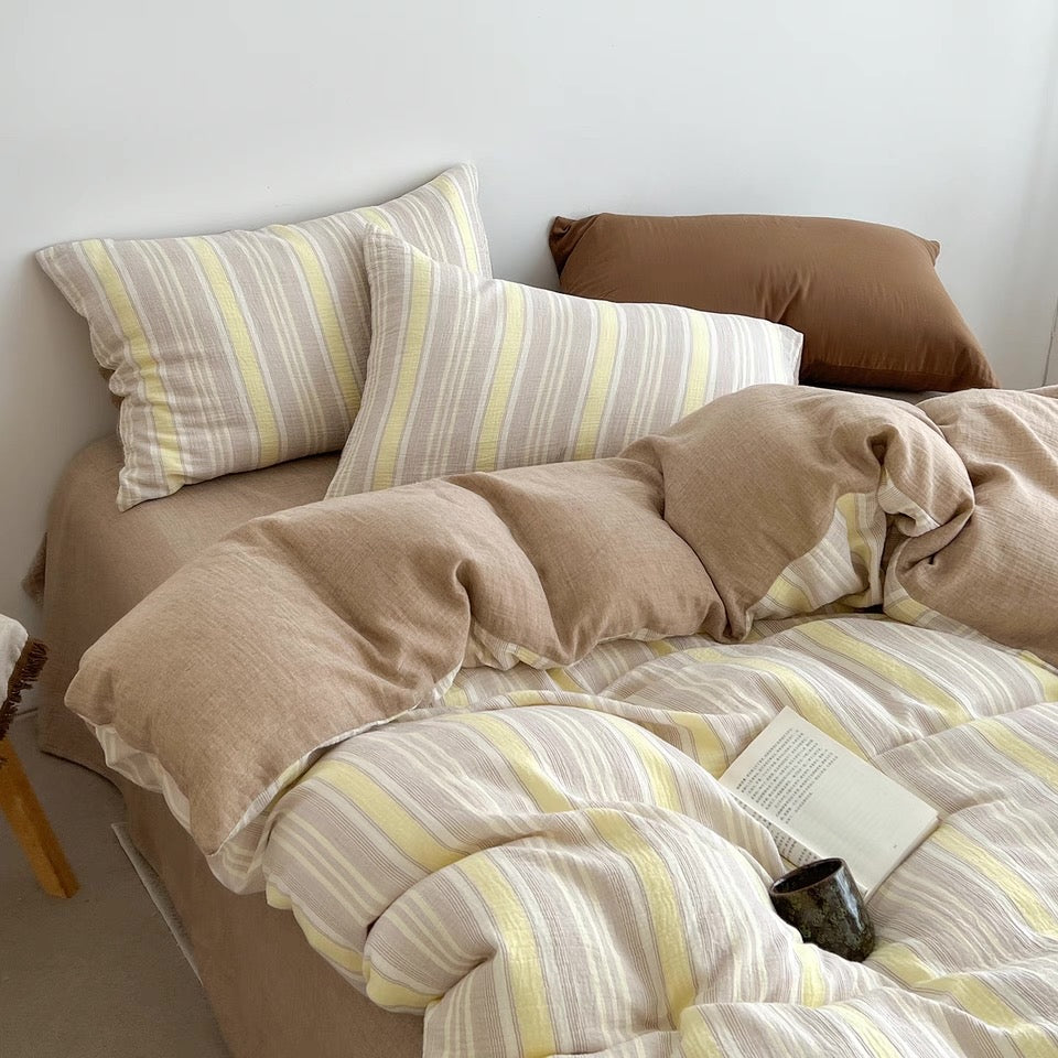 A cozy bed styled with beige and brown bedding, including a striped duvet cover and matching pillowcases, with a solid brown accent pillow in the background.