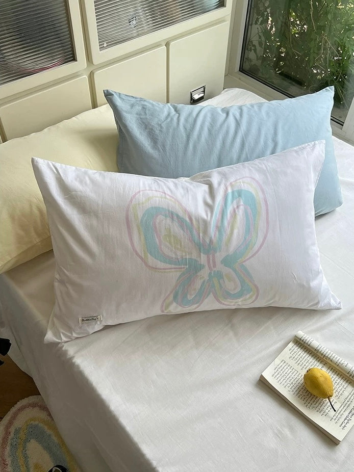Cotton pillowcase with multicolor butterfly artwork against white bedding.