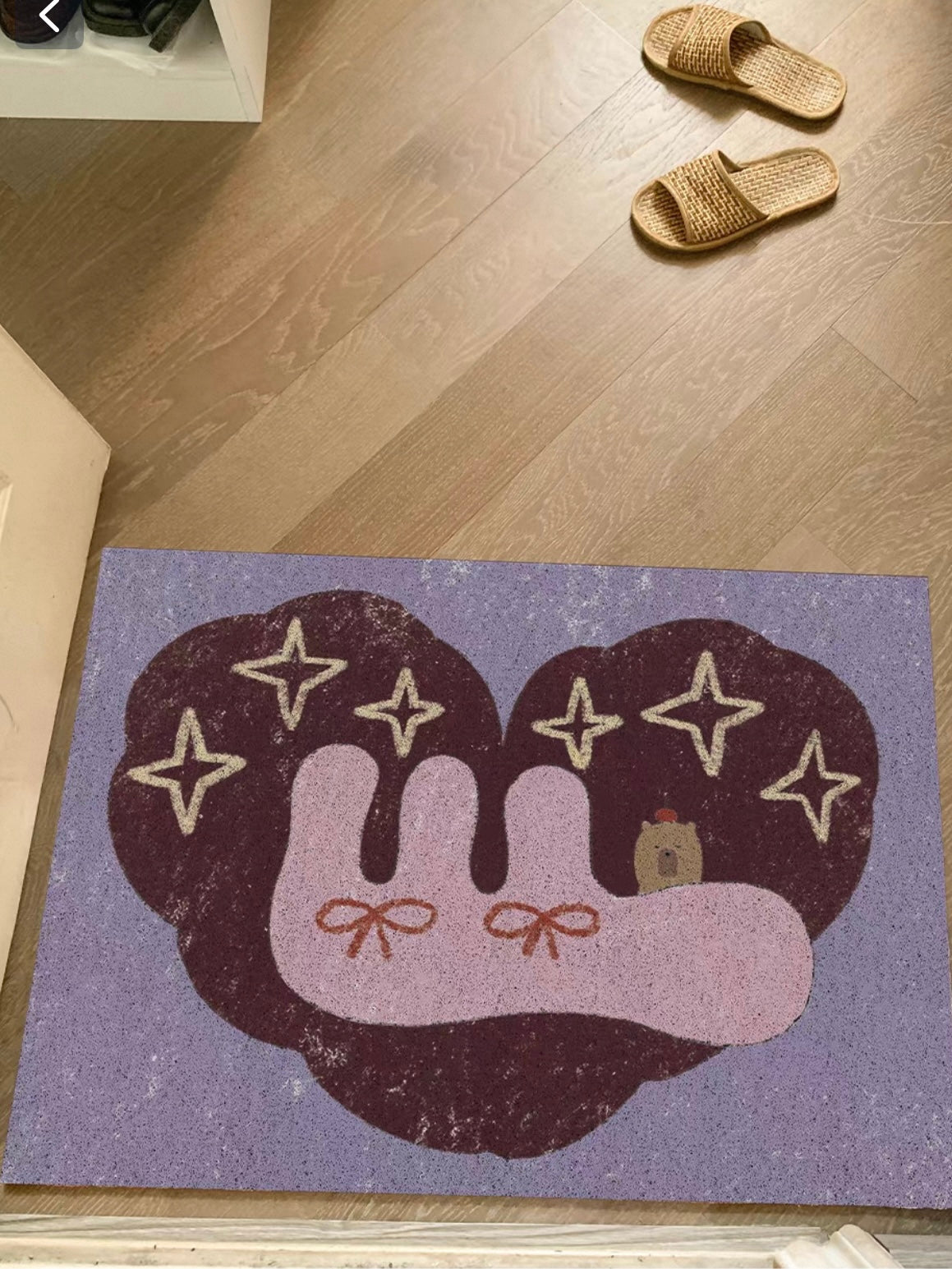 A capybara bedroom rug shows pink bow details, pale stars and a dark rounded motif on a lilac base.