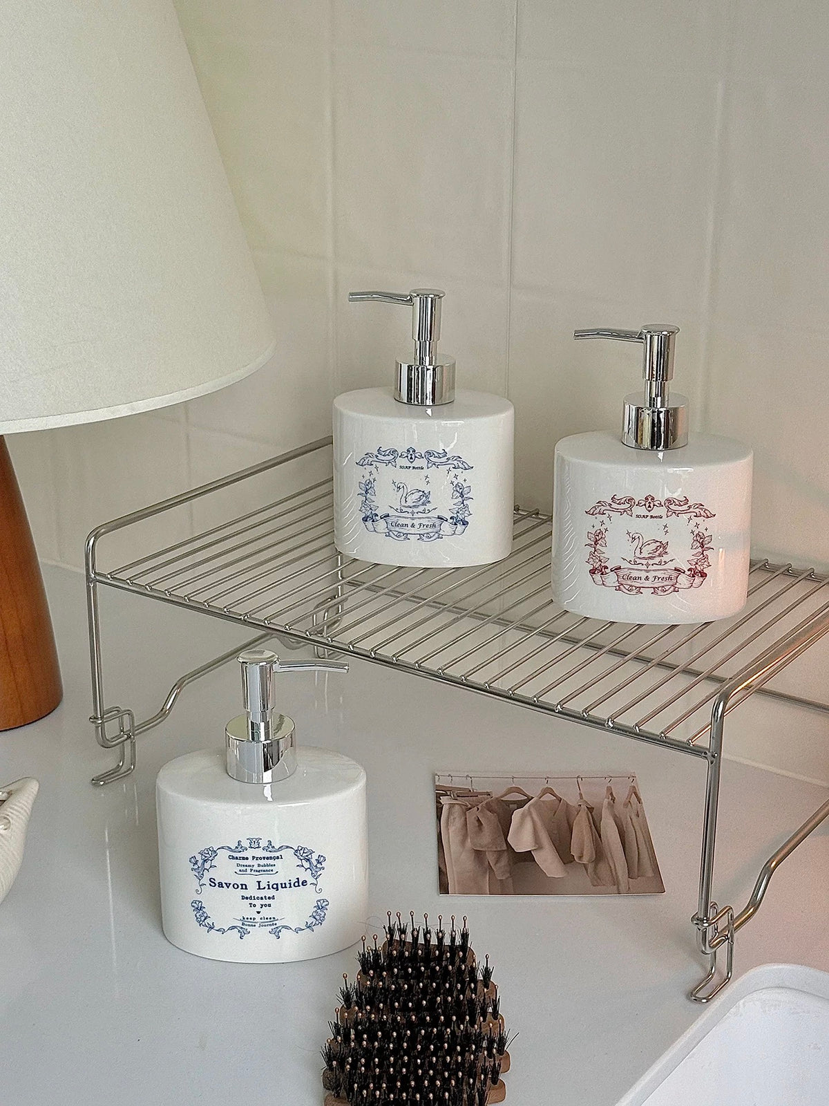 White ceramic soap dispensers with blue and red illustrations are arranged across a bathroom shelf.