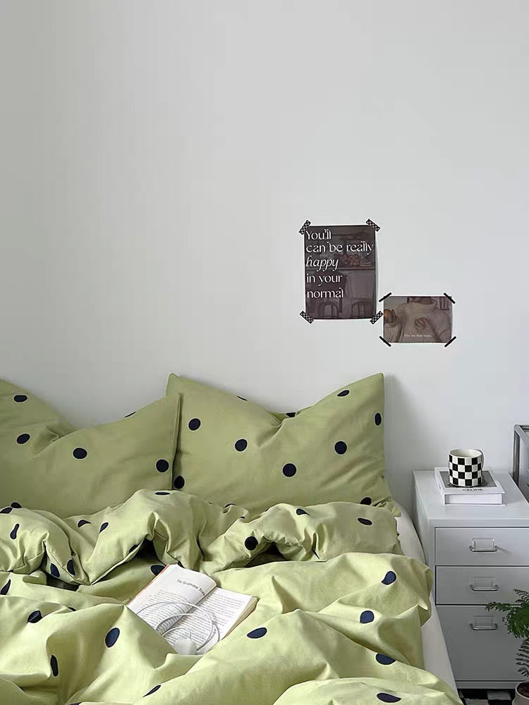 Green polka dot bedding set on a bed with a white wall and nightstand in the background.