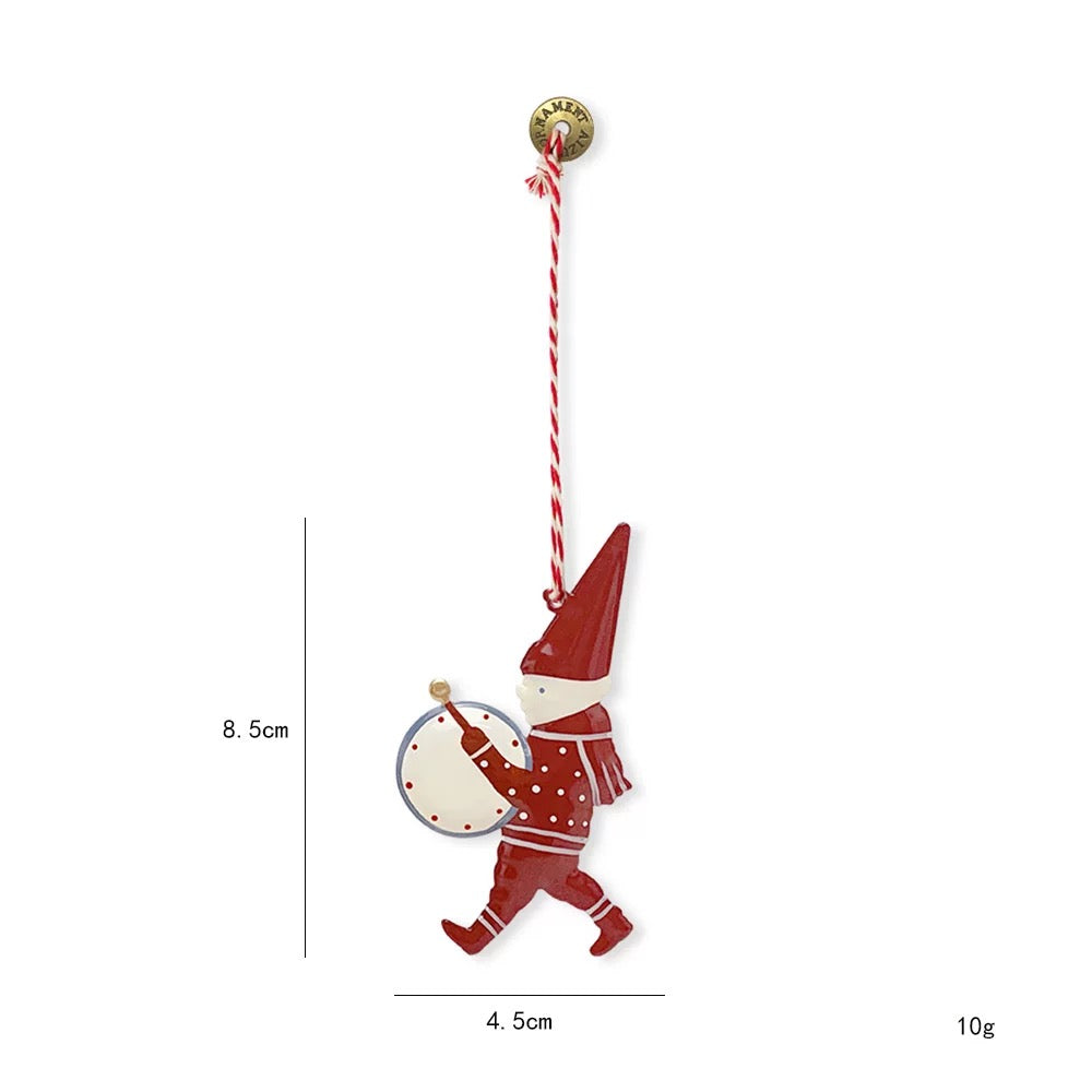 A Christmas elf ornament wears a pointed red hat and dotted outfit while holding a round white drum.