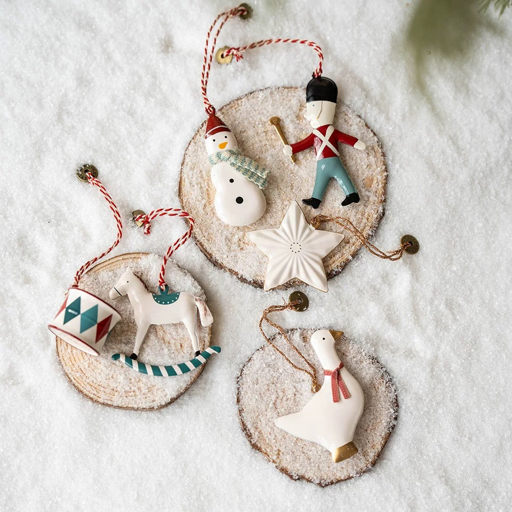 Christmas figurine ornaments include a soldier, snowman, rocking horse and white goose with a red scarf.