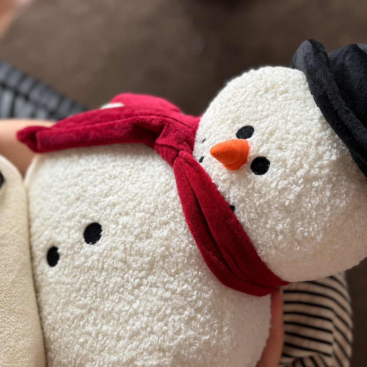 Close-up of a white snowman plush pillow with red scarf, orange nose and black hat