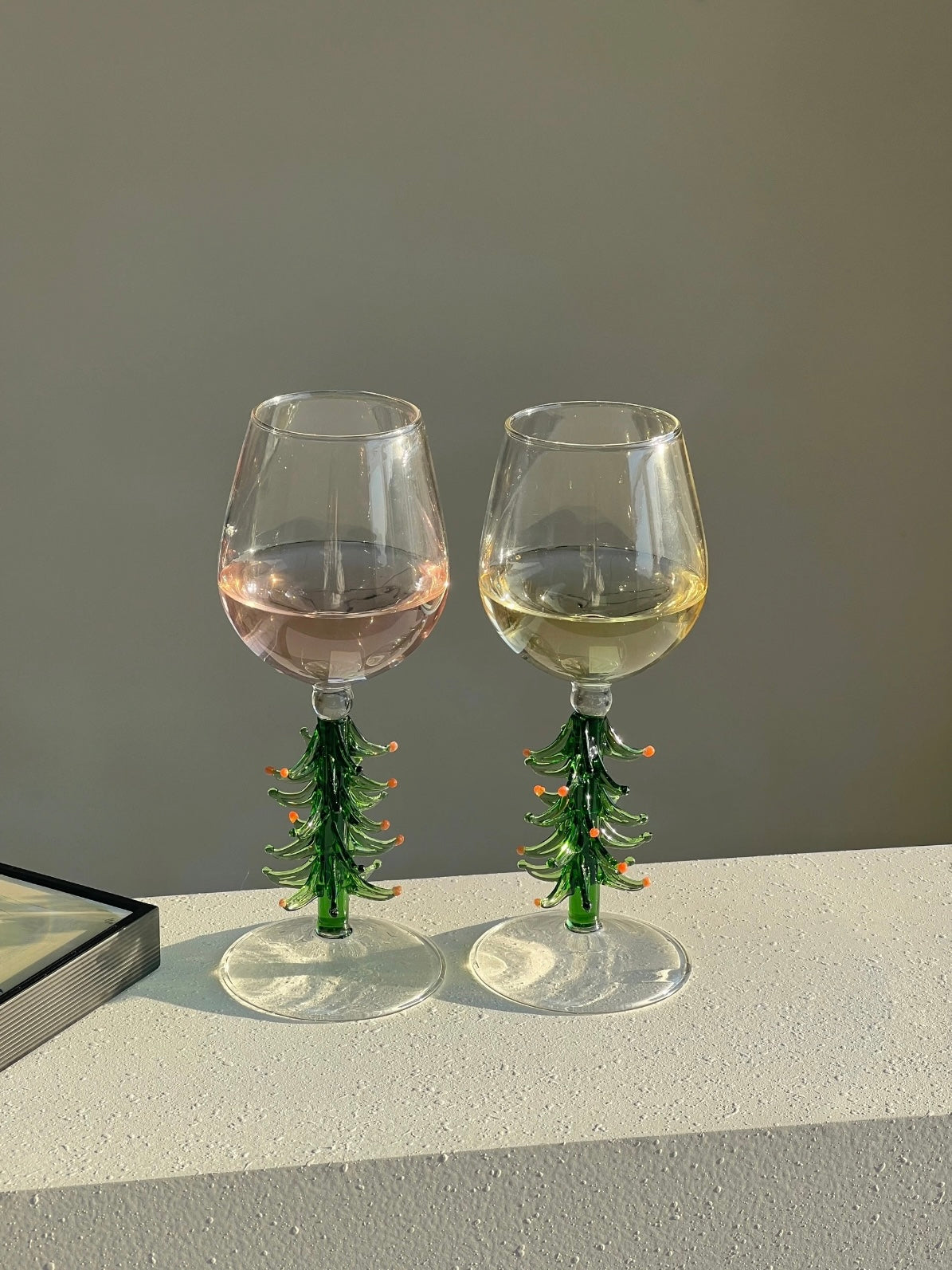 Christmas tree wine glasses with green tree stems on a neutral tabletop