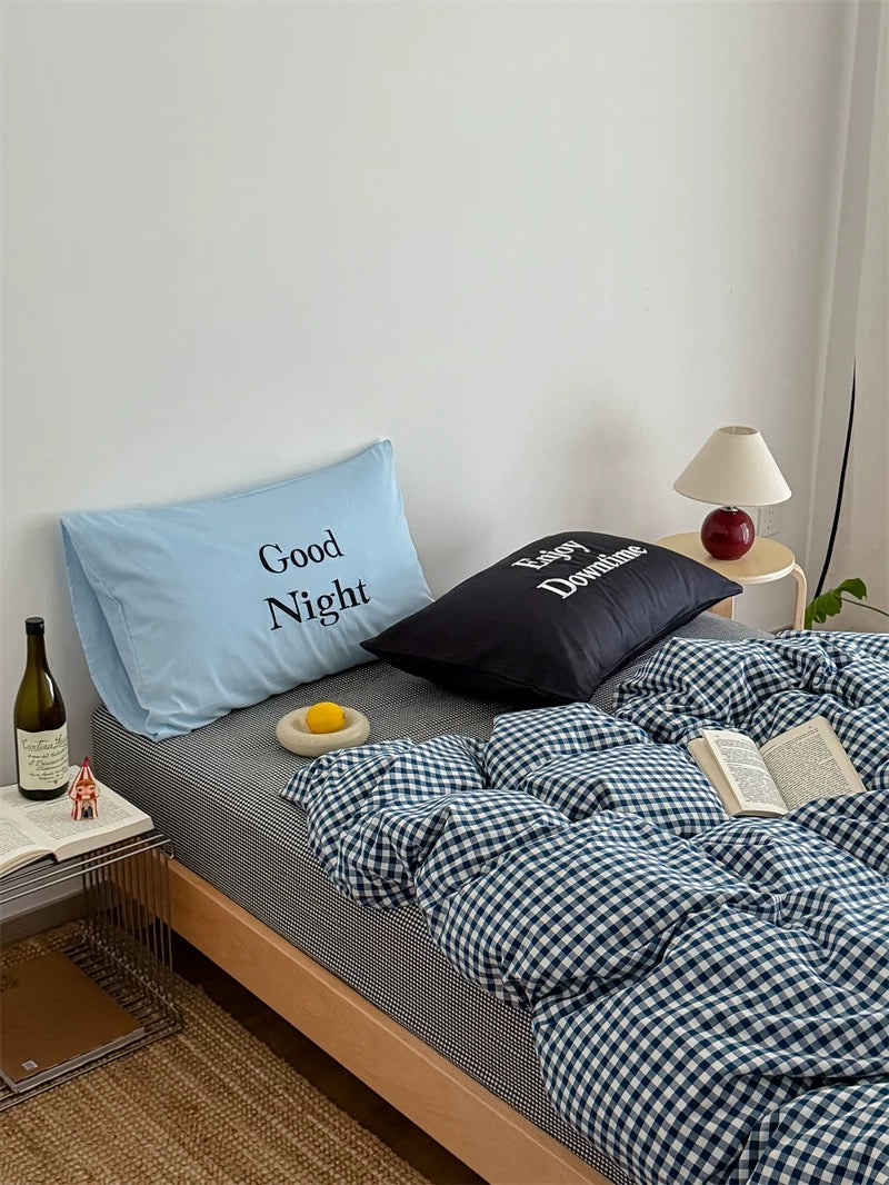 Bed with checkered duvet, pillows, and a bottle of wine on a nightstand.