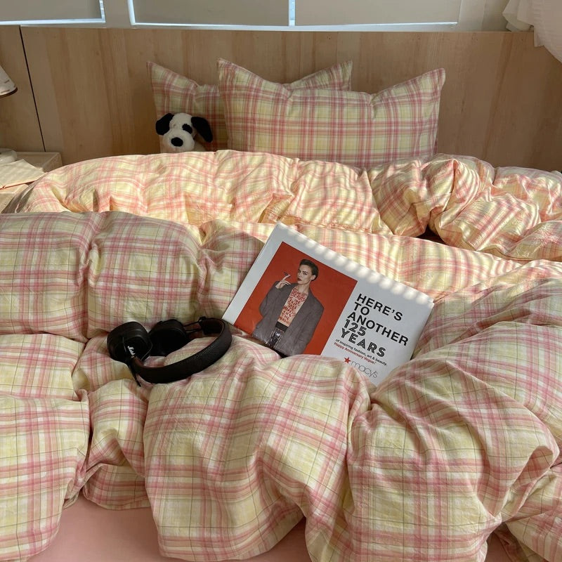 Bed with plaid bedding, a book titled 'Here's to Another Year', and headphones on a checkered pillow.