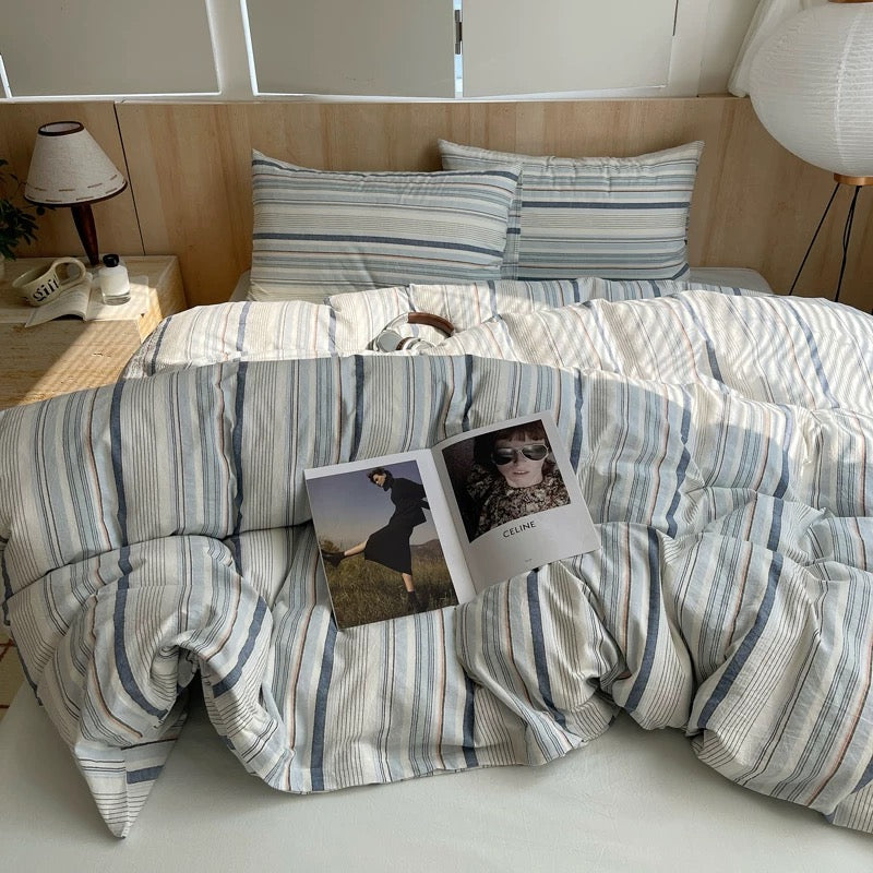 Bed with striped bedding and a lamp on a nightstand in a bedroom setting