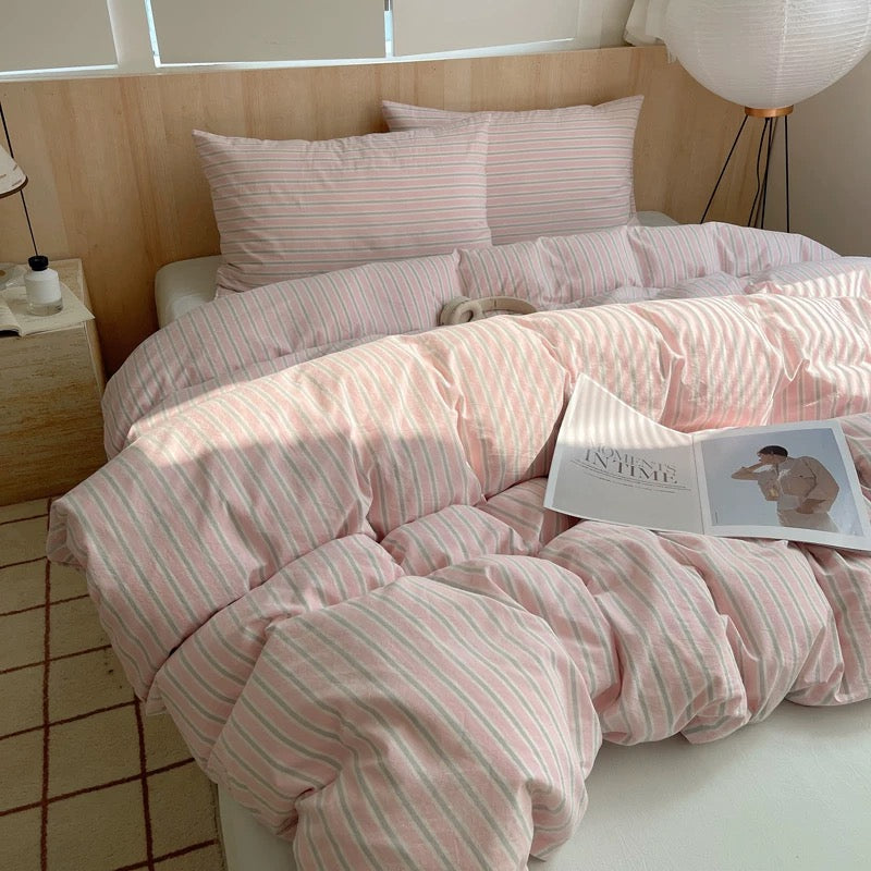 Bed with pink striped bedding and an open book on a wooden floor.
