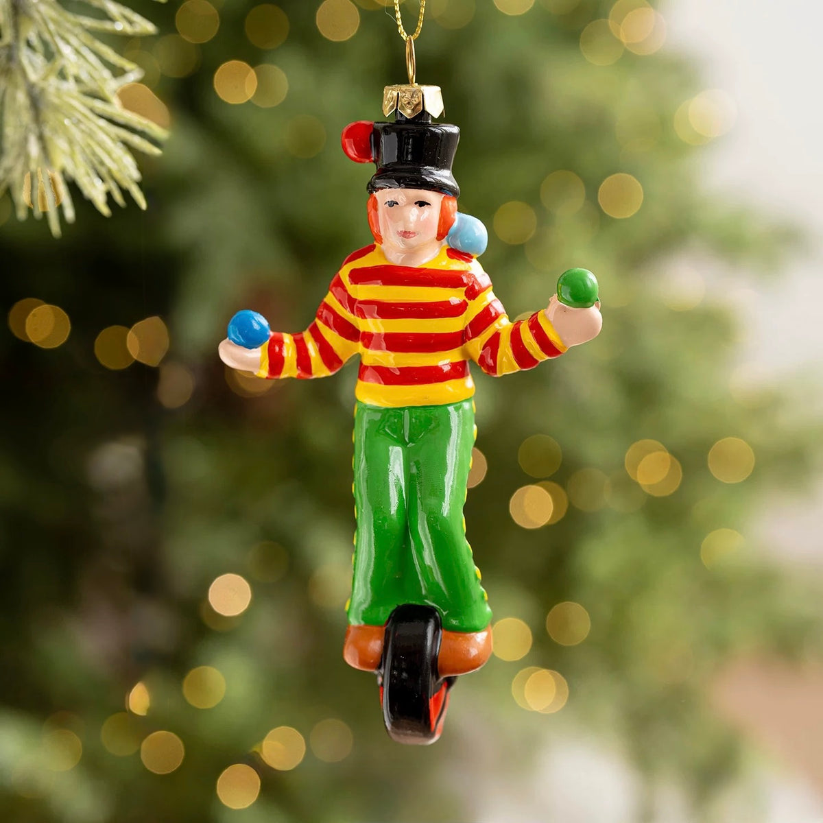 A clown ornament hangs from a gold loop with a red and yellow striped shirt, green pants and a unicycle.
