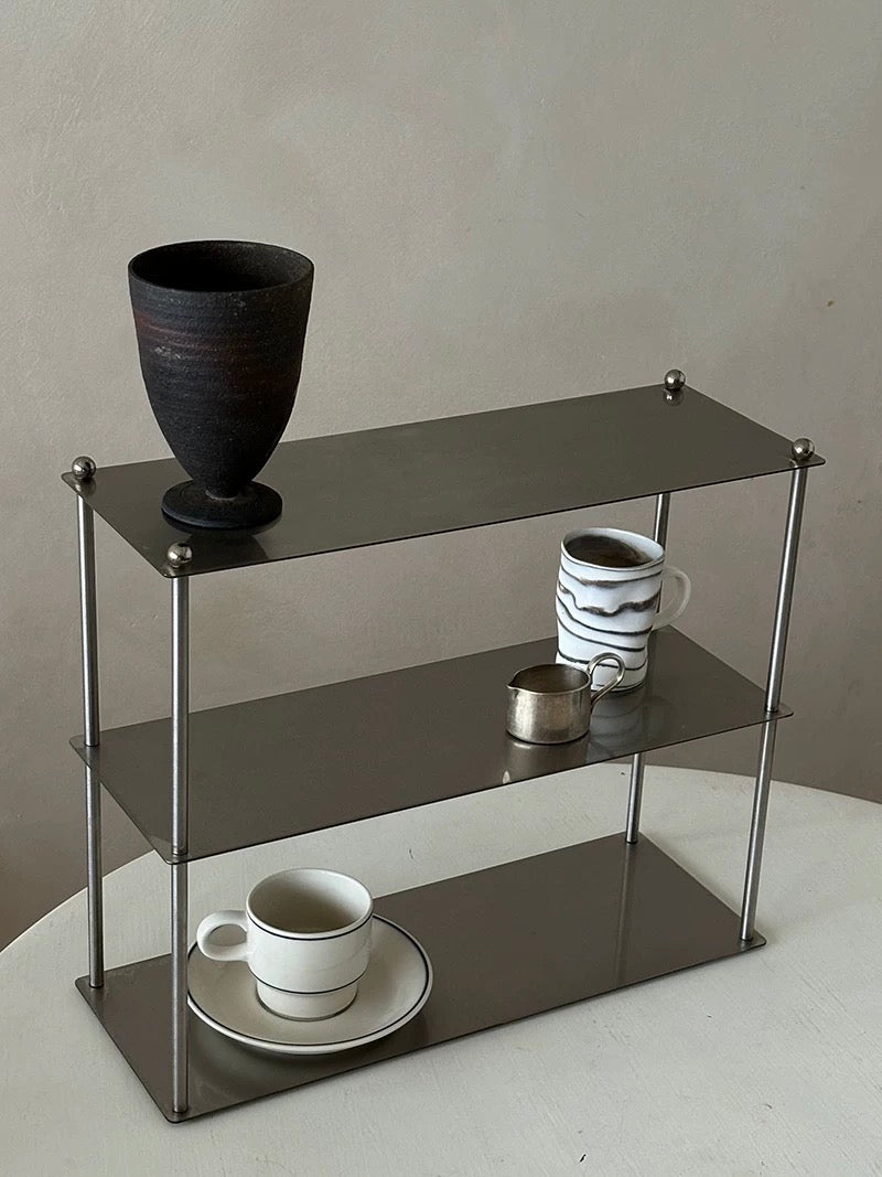 Three-tiered metal shelf with decorative items on a neutral background