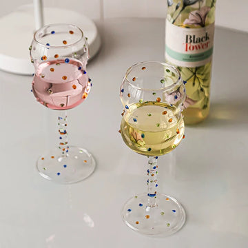 Decorative wine glasses with colorful dots on a white surface next to a bottle of 'Black Tower' wine.